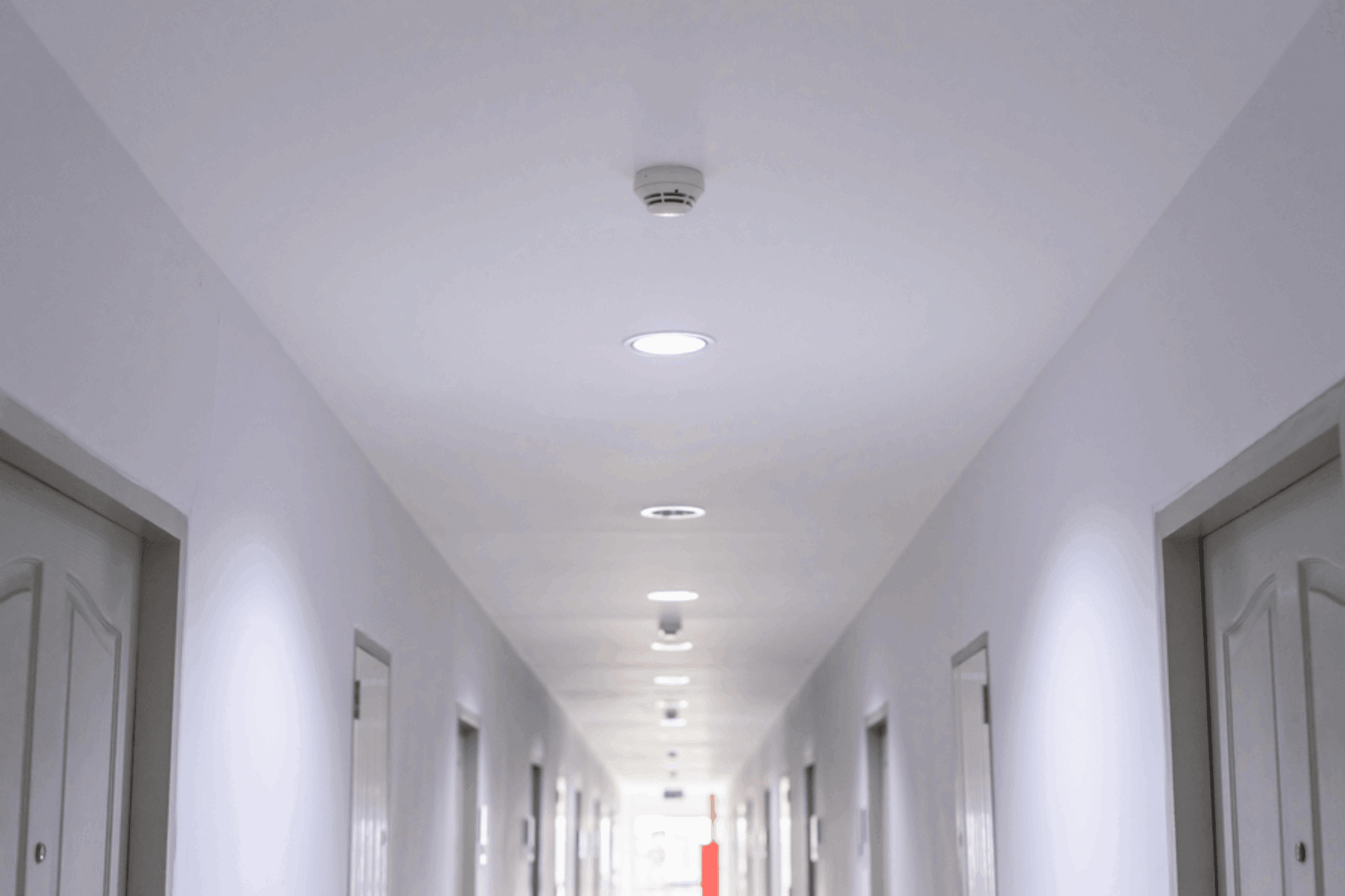 commercial building hallway with smoke detectors and recessed lights on the ceiling.