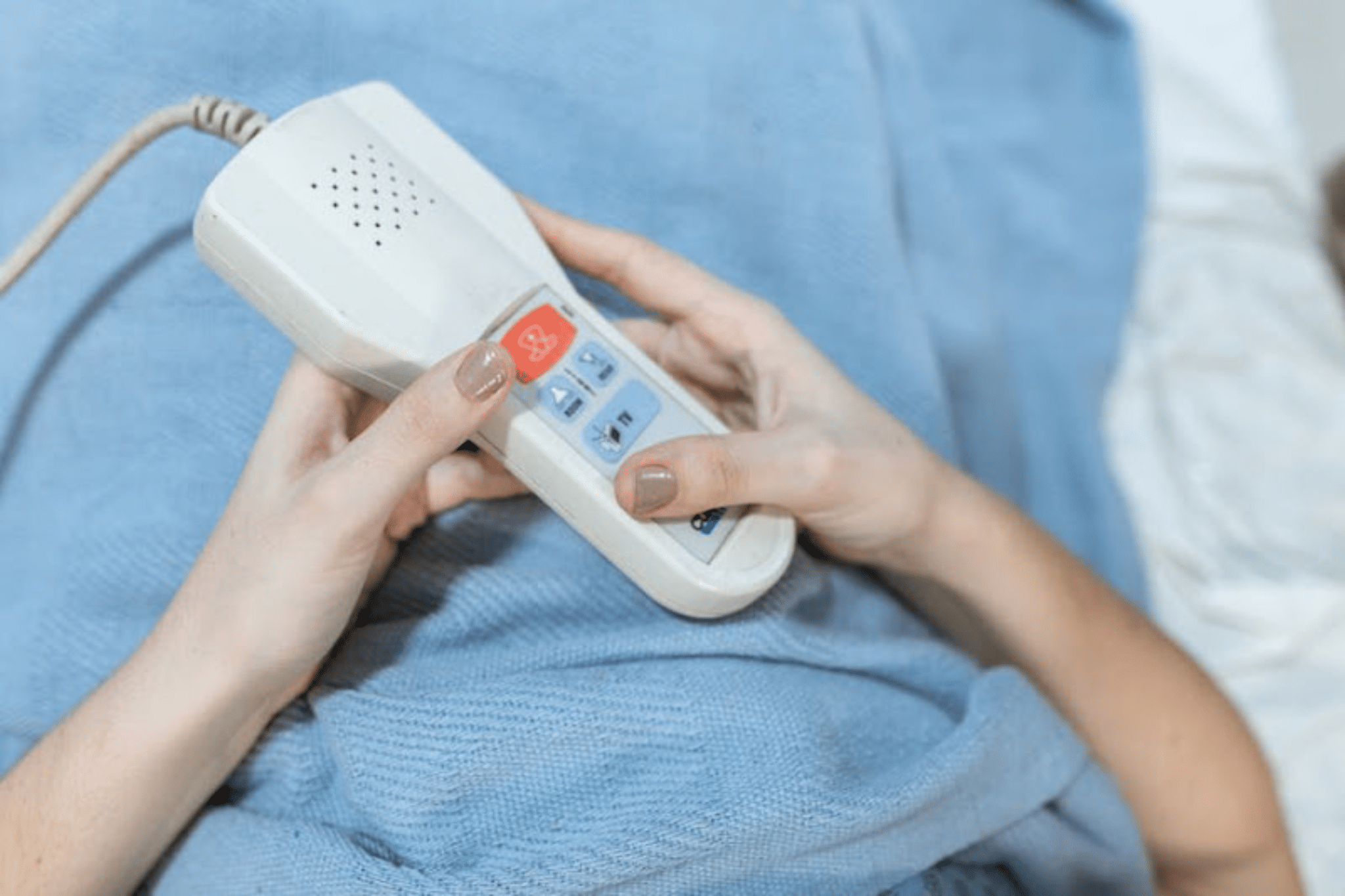 Close-up of a person holding a white nurse calling remote in a hospital bed.
